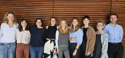 Working group Cognitive Neuroendocrinology: Nine individuals in diverse outfits stand side by side, wooden panel background.